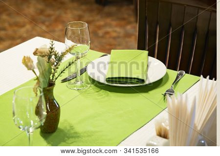 Restaurant Table Setout With White Plates, Silverware And Green Decoration