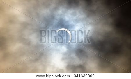 Partial Solar Eclipse Viewed Under Cloudy Skies.the Moon Covering Parts Of The Sun During A Partial 