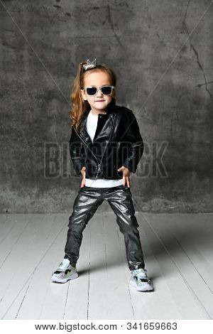 Cool Brutal Kid Girl In Leather Jacket And Shimmering Jeans Is Standing With Her Legs Wide Apart And