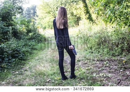 A Girl In Black With A Gun In The Nature.  Agent. Long Hair.