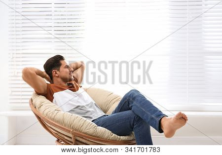 Attractive Man Relaxing In Papasan Chair Near Window At Home