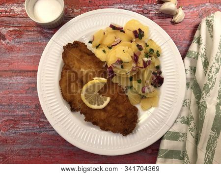 Breaded, Baked Fish Plaice Fillet With Potato Salad And Red Onions.