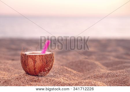 Coconut Cocktail At The Beach. Pink Straw In Coconut Set On The Sand Against The Blue Sky And Sea. C