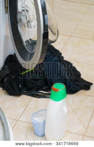 Washing Powder Liquid Detergent And Measuring Cup Next To Machine In Bathroom. Household Duties, Clo