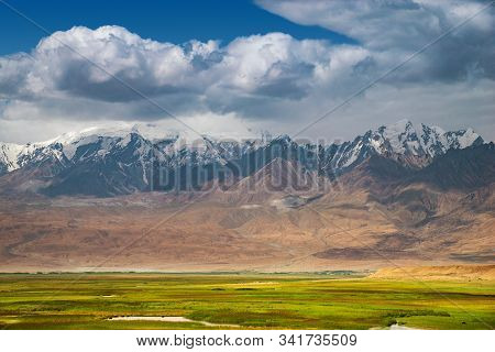 Majestic Landscape In The Pamirs Plateau With Fresh Green Meadows And Winding Rivers And Snow-capped