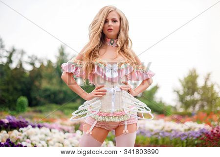 Sexy Blonde Woman Wearing Beautiful Lingerie With Stockings And Corset, Walking In Blooming Garden. 