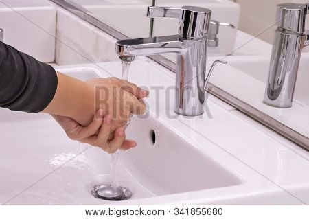 Young Girl Is Washing Her Hands Under Pouring Water From Tap In Water Closet Room With Mirror. Conce