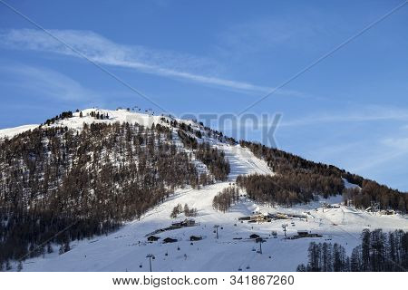 Snowy Ski Slope With Ski-lifts, Traces And Forest In High Winter Mountains At Sunny Morning. Italian