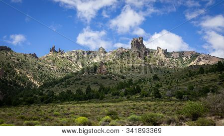 Mountain Of Rocky Peaks, Background Of Blue Sky And White Clouds. You Can See A Valley Full Of Veget