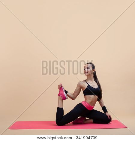 A Young Attractive Girl With A Ponytail, A Brunette, Sits In A Mermaid Pose On A Pink Yoga Mat, On A