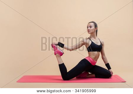 A Young Attractive Girl With A Ponytail, A Brunette, Sits In A Mermaid Pose On A Pink Yoga Mat, On A