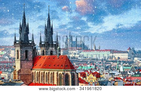 High spires towers of Tyn church in Prague city (Church of Our Lady before Tyn cathedral) urban landscape panorama with red roofs of houses in old town and blue sky with snowfall and clouds.
