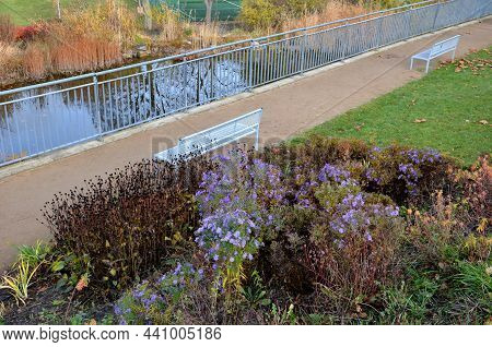 Above The Ornamental Pond In The Park Are Several Gray Metal Transparent Benches On The Park Gravel 
