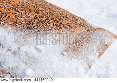 Close-up Of Carpet In Snow. Old Persian Carpet In Red Shades Of Color Is Turned Upside Down And Spri