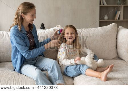 Happy Young Mother Detangling Hair Of Little Daughter.