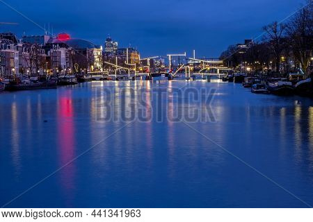 City scenic from Amsterdam at the river Amstel with the iluminated thiny bridge in the Netherlands at sunset