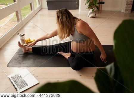 Caucasian Pregnant Female Stretching On Yoga Mat While Watching Workout Video