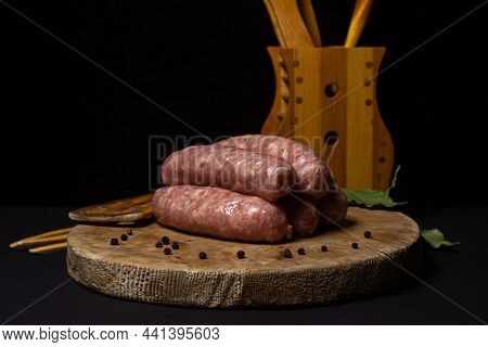 Raw Meat Sausages On A Wooden Board On A Black Background. Homemade Sausages In A Natural Casing. Me