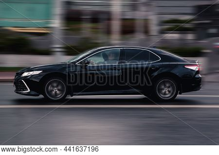 Side View Toyota Camry Xv70 Car Moving On Wet Slippery City Road. Driver In Black Sedan Rushes For J