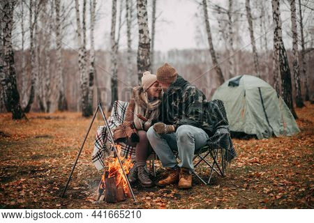 A Couple In Love In The Fall On A Camping, Sit On Chairs Near The Fire, Fry Sausages On Hats. Blonde