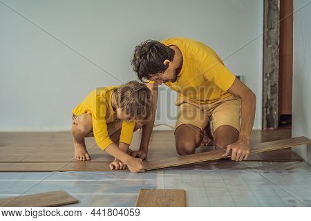 Father And Son Installing New Wooden Laminate Flooring On A Warm Film Floor. Infrared Floor Heating 