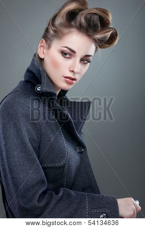 Portrait of elegant young woman in a grey overcoat  on a grey background