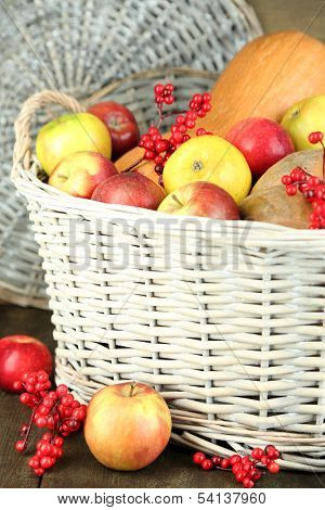 Juicy apples and pumpkin in wooden basket on table close-up