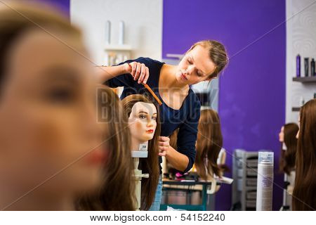 Pretty female hairdresser/haidressing apprentice/student training on an apprentice head