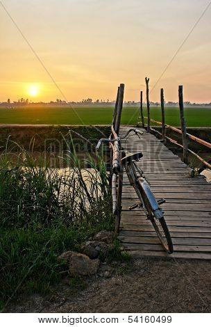 Bicycle On Wooden Fence Of Bridge At Sunset