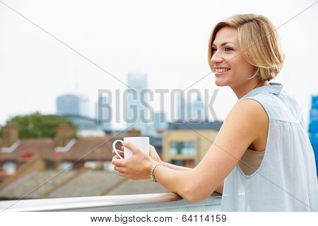 Young Woman Relaxing On Roof Terrace With Cup Of Coffee