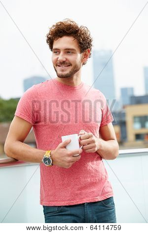 Young Man Relaxing On Roof Terrace With Cup Of Coffee