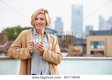 Young Woman Relaxing On Roof Terrace With Cup Of Coffee