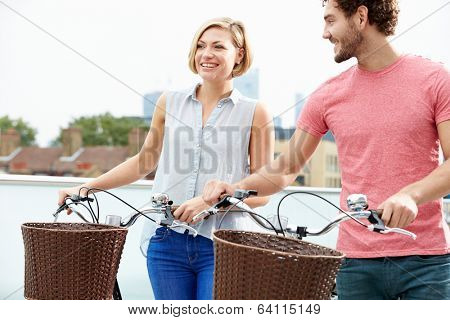 Couple Pushing Bikes With City Skyline In Background
