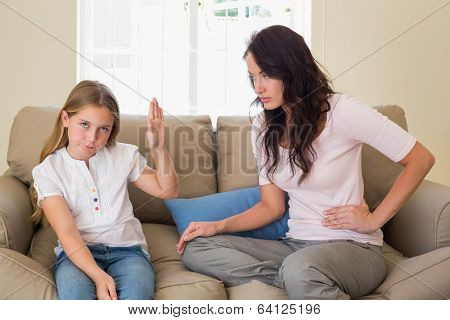 Stubborn girl showing stop gesture to mother while sitting on sofa at home