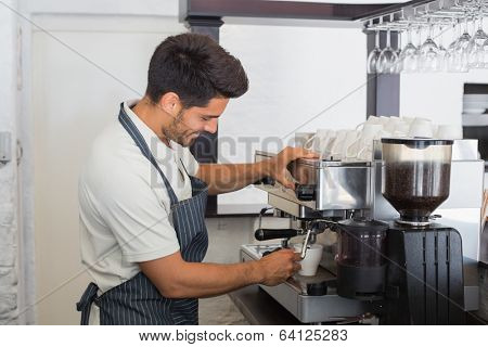 Side view of a smiling young waiter making cup of coffee at coffee shop