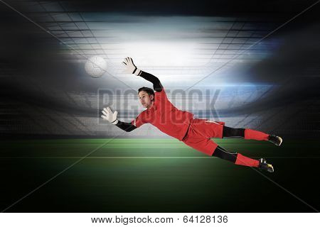 Fit goal keeper jumping up in a large football stadium with lights