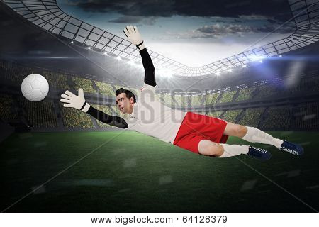 Goalkeeper in white making a save in a large football stadium with lights