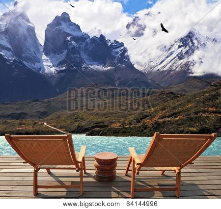 Snow-covered cliffs of Los Kuernos rise on the shores of Lake Pehoe. Two wooden chairs mounted on a wooden platform.   The magnificent national park Torres del Paine in Chile 
