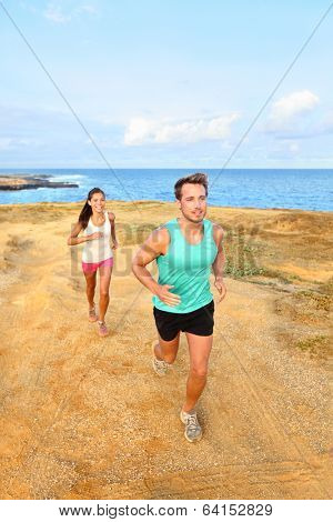 Runners running outside by ocean. Runner couple athletes, man and woman jogging outdoors in beautiful landscape on Green Sand Beach, Papakolea on Big Island, Hawaii, USA.
