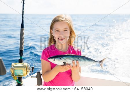 Blond kid girl fishing tuna bonito sarda fish happy with trolling catch on boat deck
