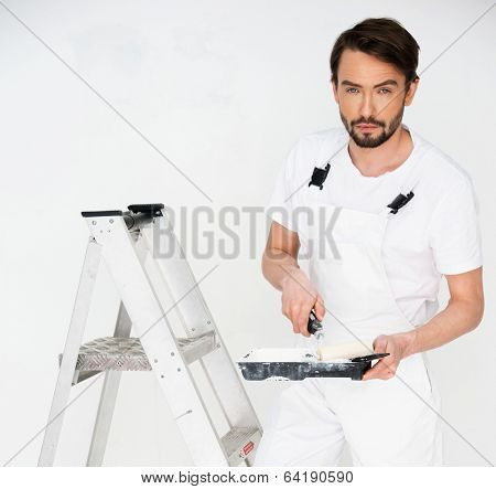 Painter standing on a stepladder holding a paint roller in his hand as he surveys a white wall, with copyspace
