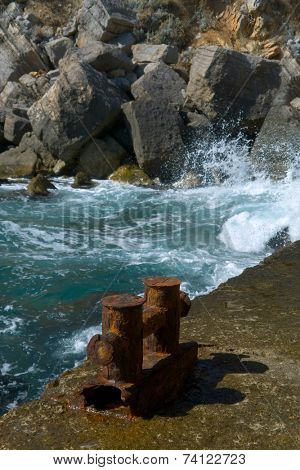 Old pier with a rusty bollard, surf on background