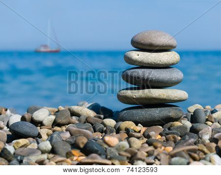 Stack of stones on beach and yacht in sea