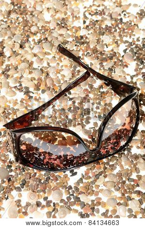 Sunglasses, lying on a white background disintegrating pebbles and sea shell beach