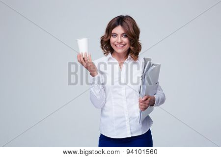 Smiling businesswoman holding folders and cup with coffee over gray background. Looking at camera
