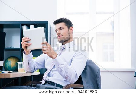 Confident businessman sitting at the table and using tablet computer in office