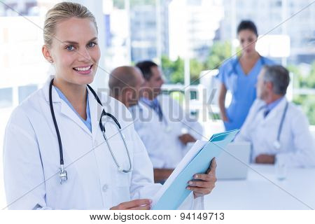 Smiling female doctor looking at camera while her colleages works in medical office