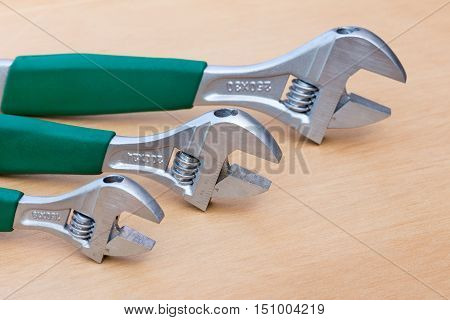 Three adjustable wrenches of different size standing upright on wood