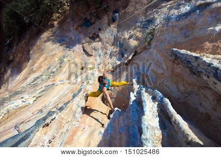 Top View of Mature Male Extreme Climber in sportive Clothing hanging on unusual shaped Rock bright Daylight Outdoors orange and blue Colors of Stone Texture