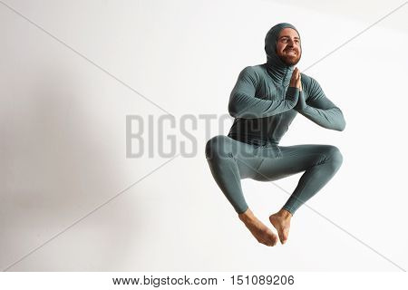 Happy smiling bearded young athlete wearing thermal baselayer suite and jumping like a ninja in air, isolated on white